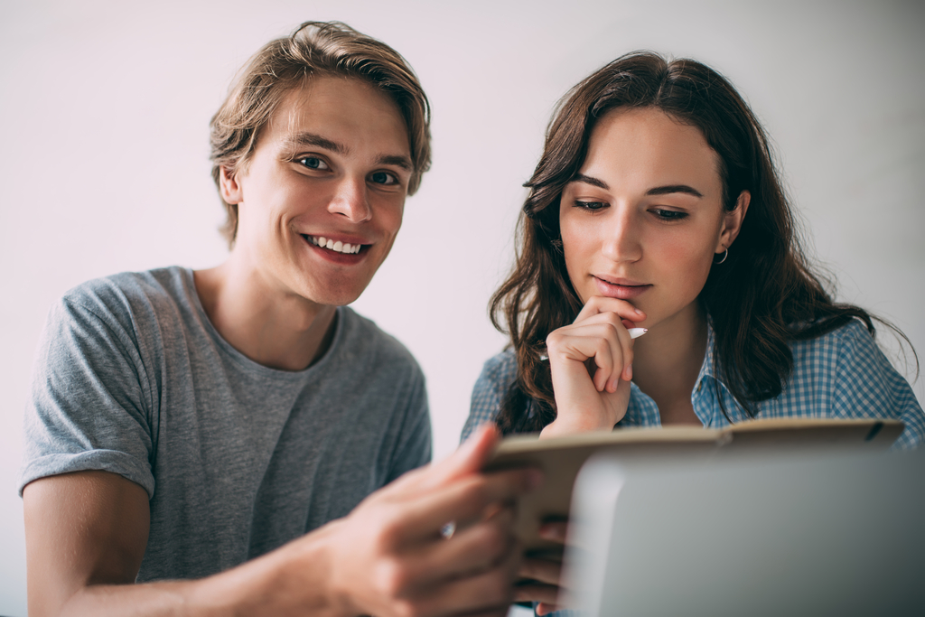 Portrait of cheerful hipster guy enjoying time for learning with female university colleague analyzing information from knowledge notebook, happy friends brainstorming on college project ideas dwoje młodych ludzi pracujących razem